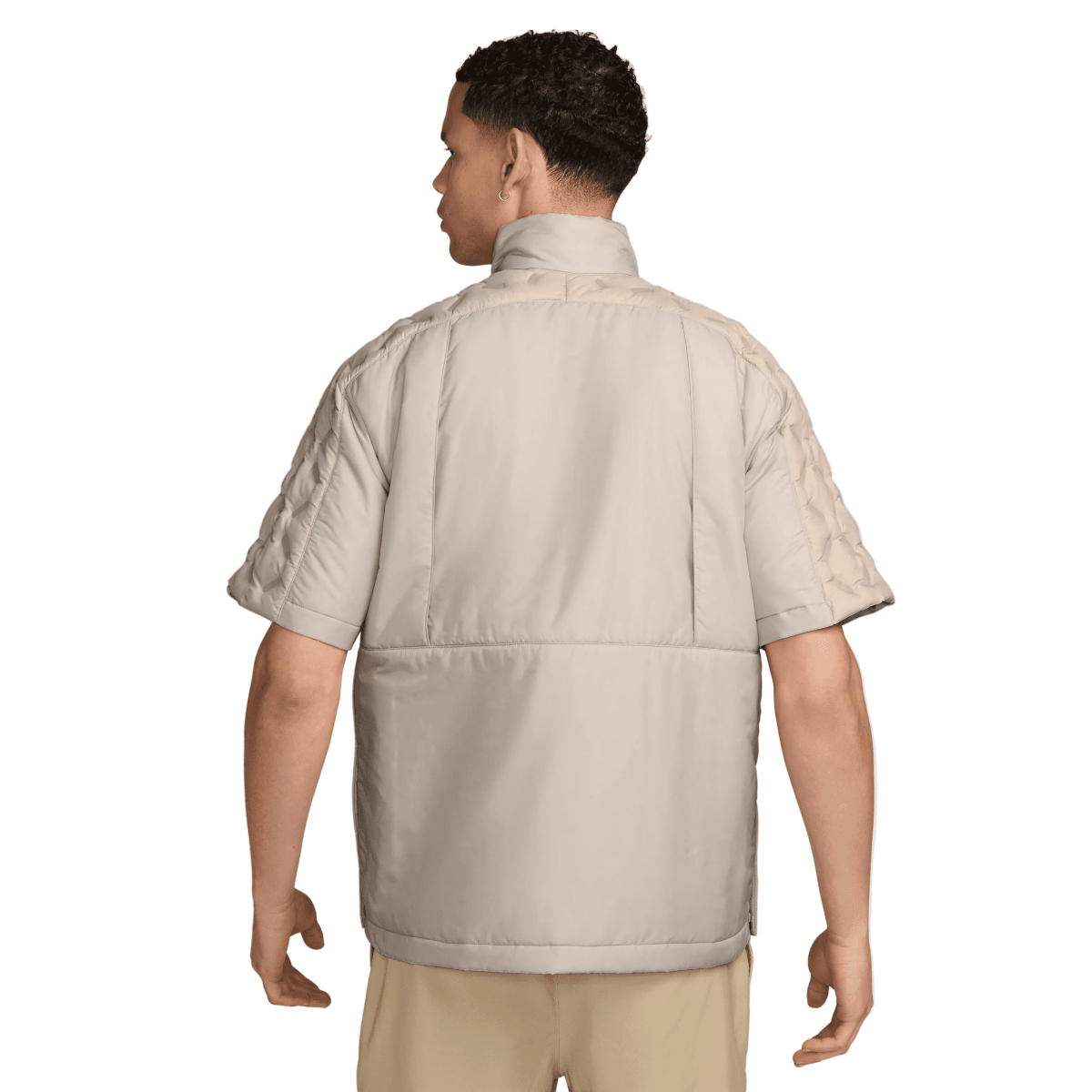 A man shown from the back wearing a light beige short-sleeve puffer jacket with quilted shoulder panels, photographed against a clean light gray studio background.